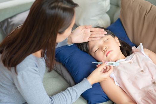 Asian mother checking her kid body temperature by thermometer which got fever and illness at home.