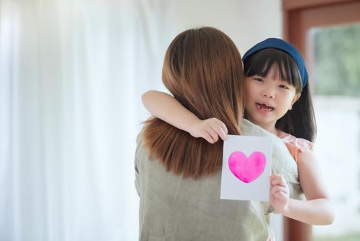 Asian mother hug her cute daughter that give handmade greeting card with colourful heart symbol to surprising her at home