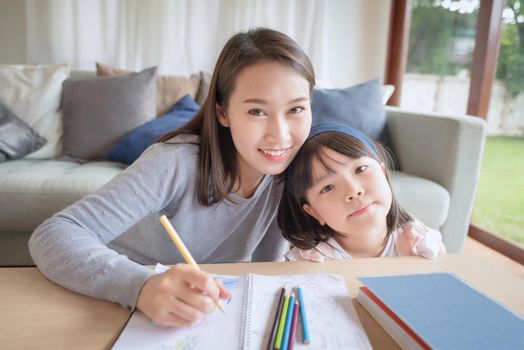Happy asian mother teaching her cute kid daughter to studying preschool in living room at home