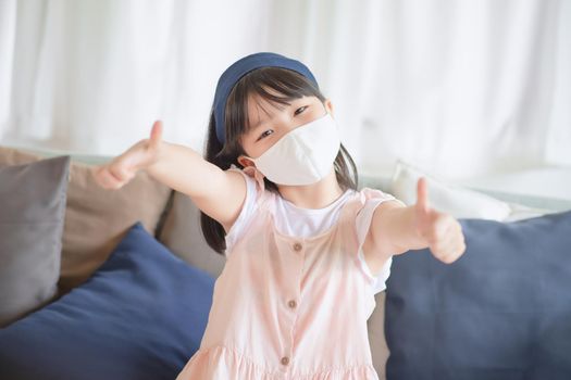 Asian little cute girl wearing hygienic face mask for prevent coronavirus or Covid-19 outbreak keep social distancing and stay at home.