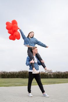 Valentines Day. Young loving couple hugging and holding red heart shaped balloons outdoors