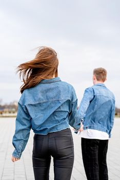 Young loving couple wearing jeans spending time together in the park having fun, woman holding hands with her boyfriend looking back