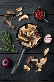 Dried porcini mushrooms set in cast iron frying pan, on black wooden table background, top view flat lay