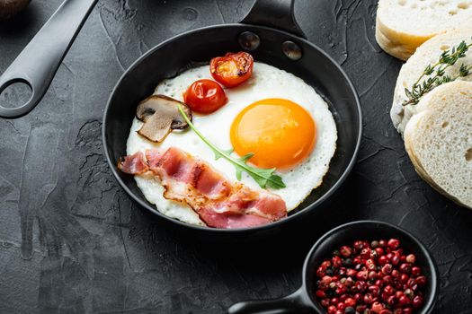 Fried eggs with bacon and vegetables set in cast iron frying pan, on black background