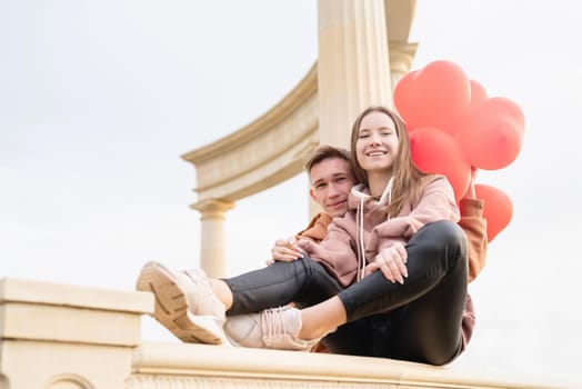 Happy young loving couple embracing each other outdoors in the park having fun holding red balloons