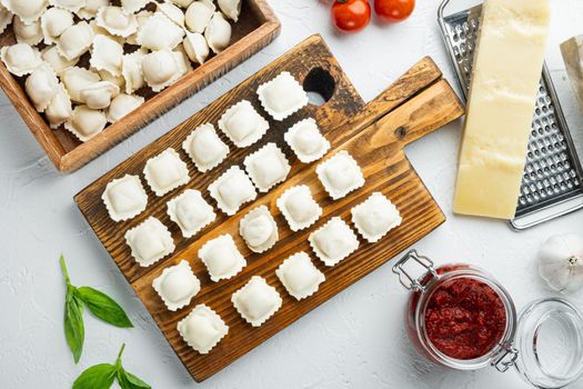 Raw Italian ravioli tortellini with fresh parmesan and basil , tomatoes set on wooden board, on white background, top view flat lay