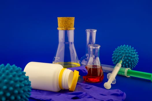 Concept of research for a Covid-19 vaccine with a conical lab flasks with yellow and red solutions alongside a hypodermic syringe and blue virus molecules over a blue background with copy space