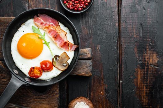 Scrambled eggs in frying pan with pork lard, bread and green feather in cast iron frying pan, on old dark wooden table background, top view flat lay , with space for text copyspace