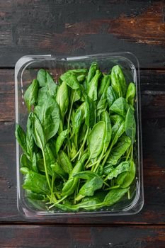 Fresh spinach set, on old dark wooden table background, in plastic pack, top view flat lay