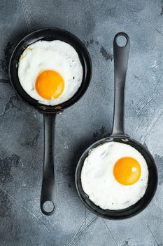 Fried eggs with cherry tomatoes and bread for breakfast in cast iron frying pan, on gray background, top view flat lay