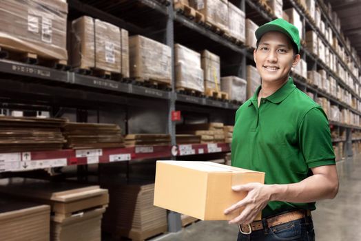 Asian delivery man or passenger holding a cardboard box with logistics warehouse in background