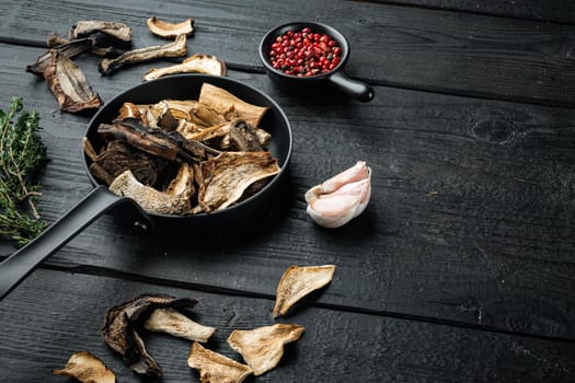 Dried wild mushrooms set in cast iron frying pan, on black wooden table background , with space for text copyspace