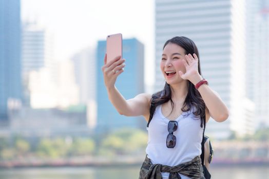Beautiful asian tourist woman use video call via a smartphone in urban city downtown. Vacation travel in summer.