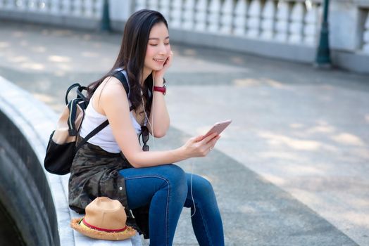 Beautiful asian tourist woman relaxing and enjoying listening the music on a smartphone in urban city downtown. Vacation travel in summer.