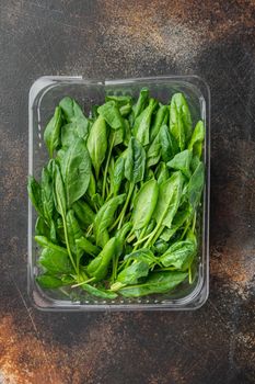 Washed fresh mini spinach set, on old dark rustic background, in plastic pack, top view flat lay