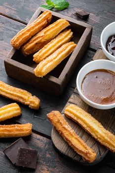 Typical Spanish snack churros, fried-dough pastry served usually with chocolate caramel hot sauce set, on old dark wooden table background
