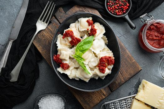 Appetizing ravioli with tomato sauce, cheese and basil set with basil parmesan and tomatoe in black bowl, on gray background, top view flat lay