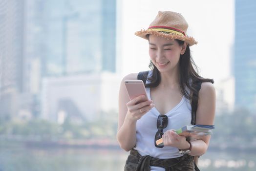 Beautiful asian solo tourist woman  smiling and looking at mobile phone for searching tourists sightseeing spot. Vacation travel in summer.