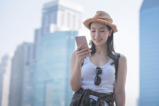 Beautiful asian solo tourist woman smiling and looking at mobile phone for searching tourists sightseeing spot. Vacation travel in summer