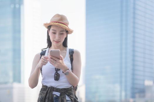 Beautiful asian solo tourist woman smiling and looking at mobile phone for searching tourists sightseeing spot. Vacation travel in summer