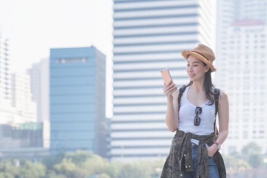 Beautiful asian solo tourist woman smiling and looking at mobile phone for searching tourists sightseeing spot. Vacation travel in summer