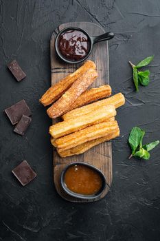 Typical Spanish snack churros, fried-dough pastry served usually with chocolate caramel hot sauce set, on black background, top view flat lay