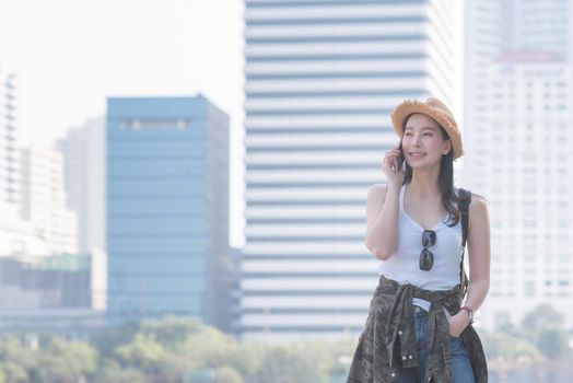 Beautiful asian solo tourist woman smiling and enjoy taking via mobile phone in city downtown. Vacation travel in summer.