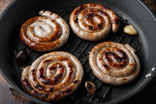 Fried Bavarian pork meat spiral sausages set in cast iron frying pan, on old dark rustic background