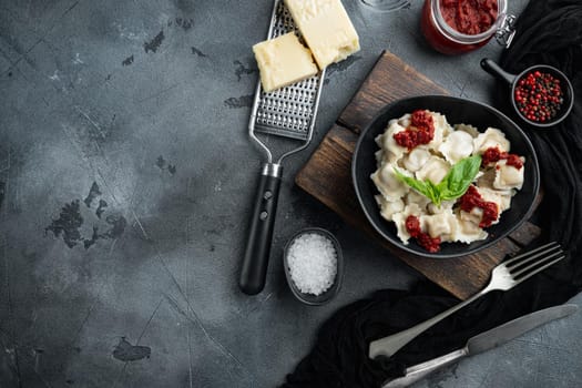 Appetizing ravioli with tomato sauce, cheese and basil set with basil parmesan and tomatoe in black bowl, on gray background, top view flat lay , with copyspace and space for text