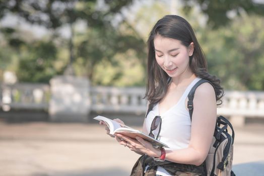 Beautiful asian tourist woman reading the travel guide book searching for for tourists sightseeing spot. Vacation travel in summer.