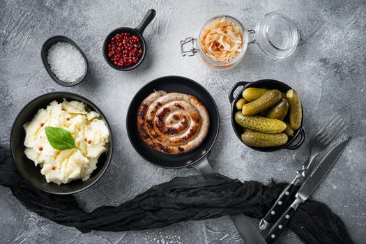 Fried Bavarian German Nurnberger sausages with sauerkraut, mashed potatoe in cast iron frying pan, on gray background, top view flat lay