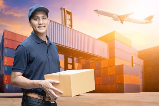 Asian delivery man holding a cardboard box with logistics yard background for e-commerce and logistics concept.