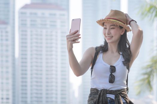 Beautiful asian tourist woman taking selfies on a smartphone in urban city downtown. Vacation travel in summer.