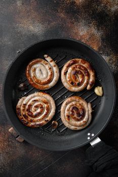 Grilled pork meat sausages set in cast iron frying pan, on old dark rustic background, top view flat lay