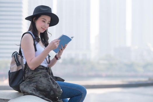 Beautiful asian tourist woman reading the travel guide book searching for for tourists sightseeing spot. Vacation travel in summer.