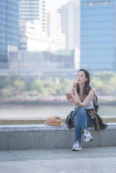 Beautiful asian solo tourist woman relaxing and enjoying listening the music on a smartphone in urban city downtown. Vacation travel in summer.