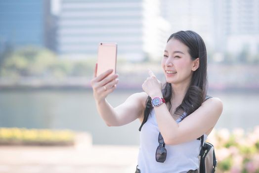 Beautiful asian woman enjoy using video call technology on a smartphone in urban city downtown. Vacation travel in summer.