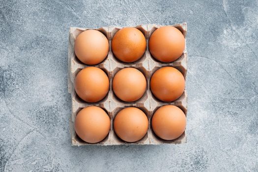 Raw chicken eggs in egg box set on gray background, top view flat lay