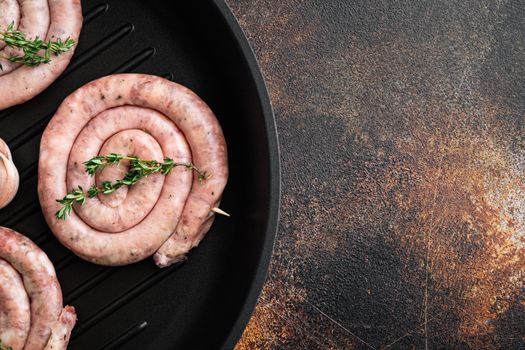 Traditional raw spiral pork sausages set in cast iron frying pan, on old dark rustic background, top view flat lay , with space for text copyspace