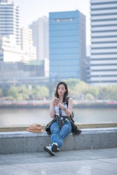 Beautiful asian tourist woman relaxing and enjoying listening the music on a smartphone in urban city downtown. Vacation travel in summer.