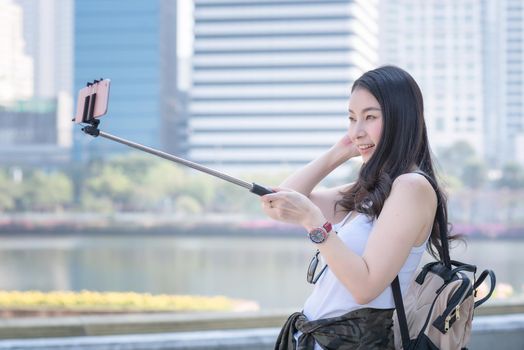 Beautiful asian tourist woman taking selfies on a smartphone in urban city downtown. Vacation travel in summer.