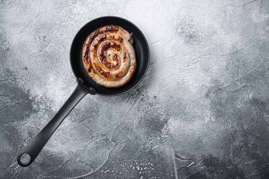 Grilled Spiral sausage set in cast iron frying pan, on gray background, top view flat lay , with space for text copyspace