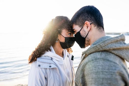 New normal couple in love issues due to social social distancing: man and girlfriend looking in the eyes each other head to head with setting sun reflection on the sea water. Focus on woman eye