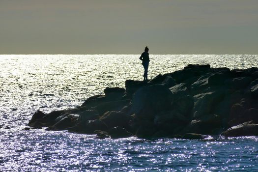 Alone female silhuette standing on cliff by the sea