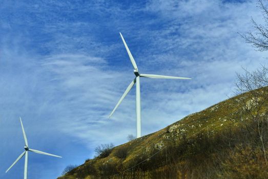 Wind turbine in natural environment near high voltage pylon