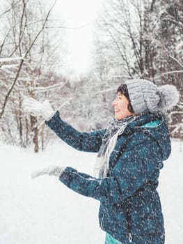 Smiling woman is playing with snow. Fun in snowy winter forest. Woman laughs as she walks through wood. Sincere emotions.