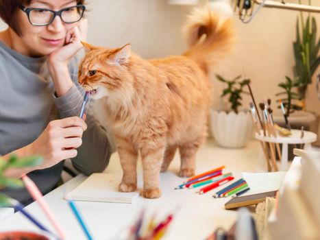 Woman with short hair cut is drawing in notebook. Cute ginger cat sits near her. Fluffy pet and artist. Calming hobby, anti stress leisure.