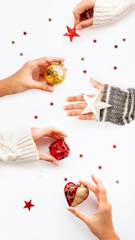 Hands with New Year decoration - red heart, golden ball, white star on white background. Top view on decoration for Christmas tree. Vertical banner 9:16.