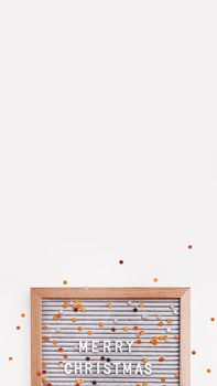 Letter board with Merry Christmas greeting and scattering golden confetti. New Year celebration. Copy space on white background. Vertical banner 9:16.