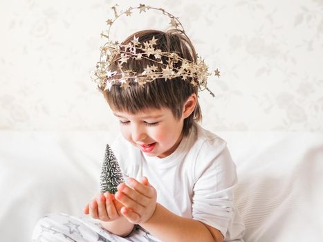 Joyful boy is playing with decorations for Christmas tree. Funny kid is ready for New Year celebration. Cozy home. Winter holiday spirit.